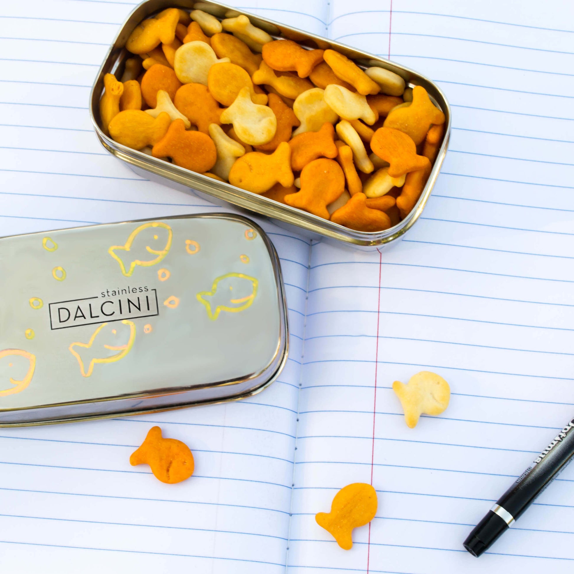 Goldfish crackers in stainless steel snack box on top of lined notebook