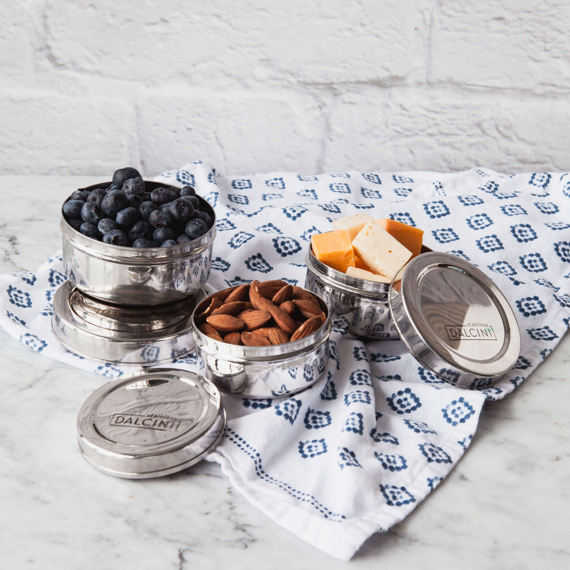 almonds, blueberries, and cheese in 3 round stainless steel snack boxes on a kitchen cloth