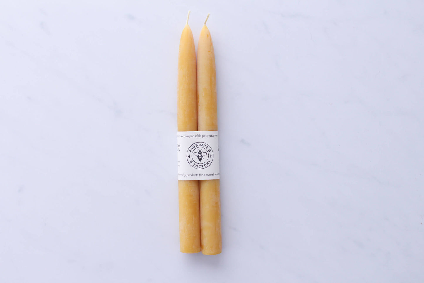 Set of 2 handmade beeswax taper candles wrapped in cardboard ring packaging with B Factory logo 