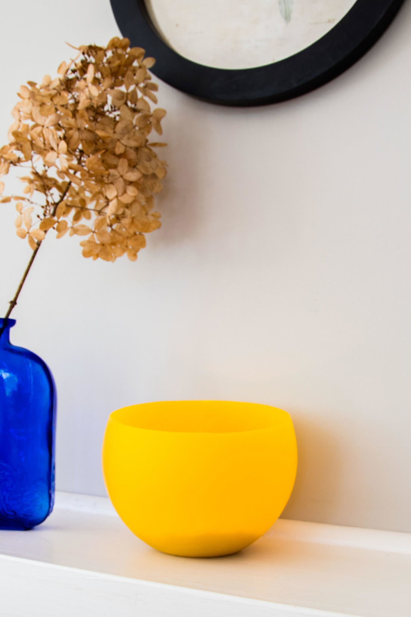 Handmade beeswax luminary on living room shelf next to dried hydrangeas in blue vase