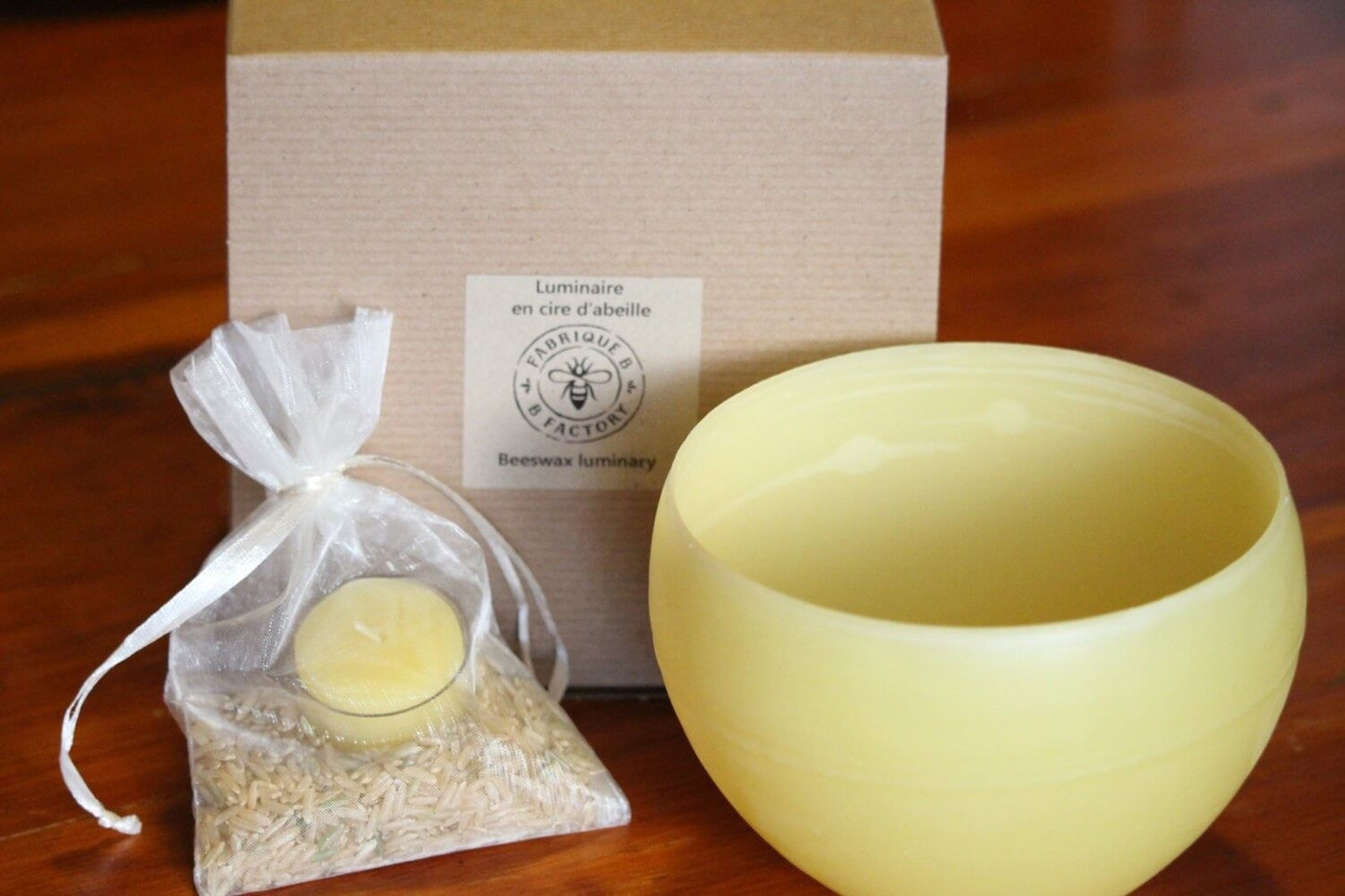 Beeswax luminary next to bag of brown rice, beeswax tea light candle in glass cup, and gift box with B Factory logo