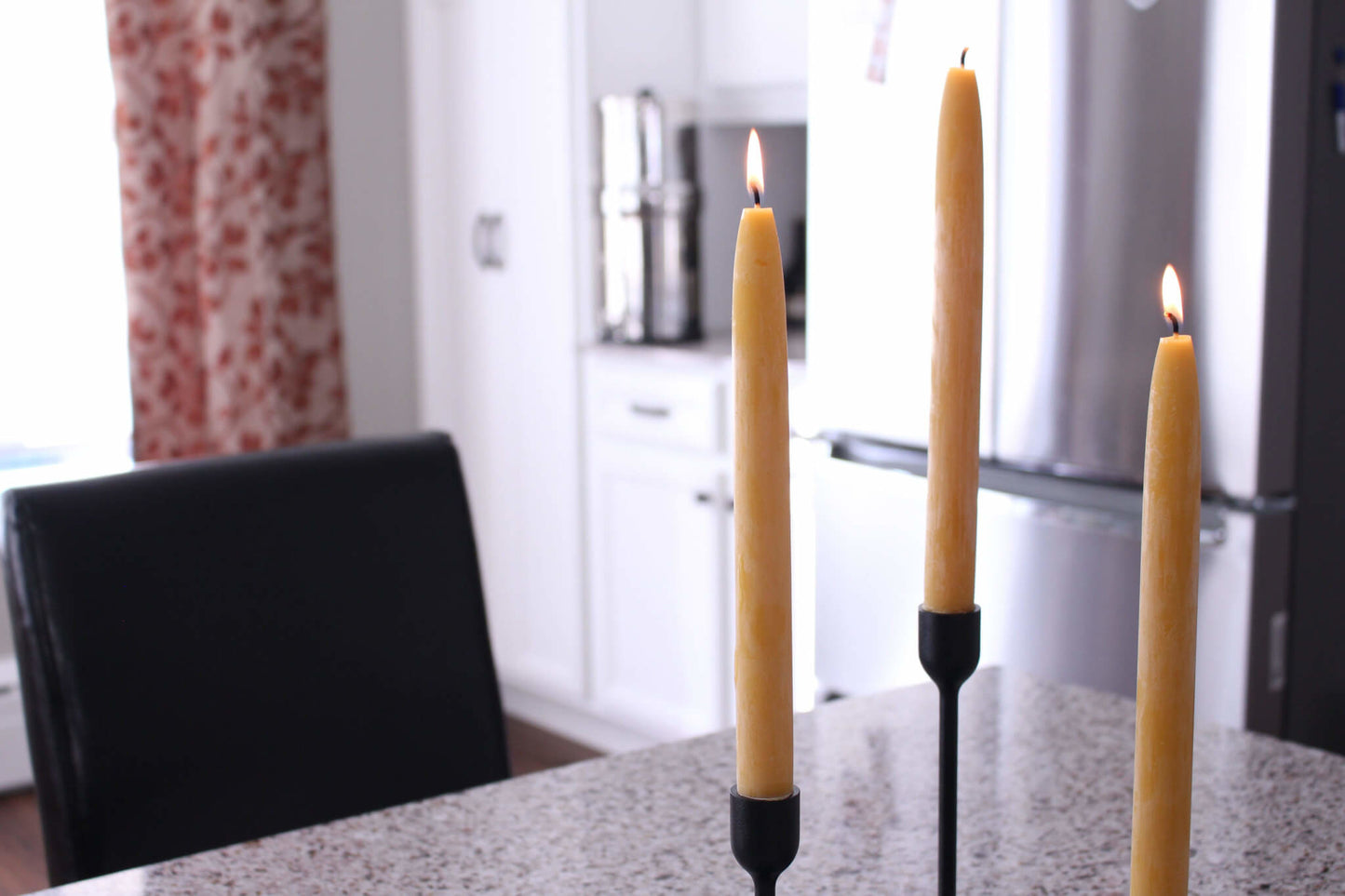 3 lit taper beeswax candles in black candle holders on kitchen table