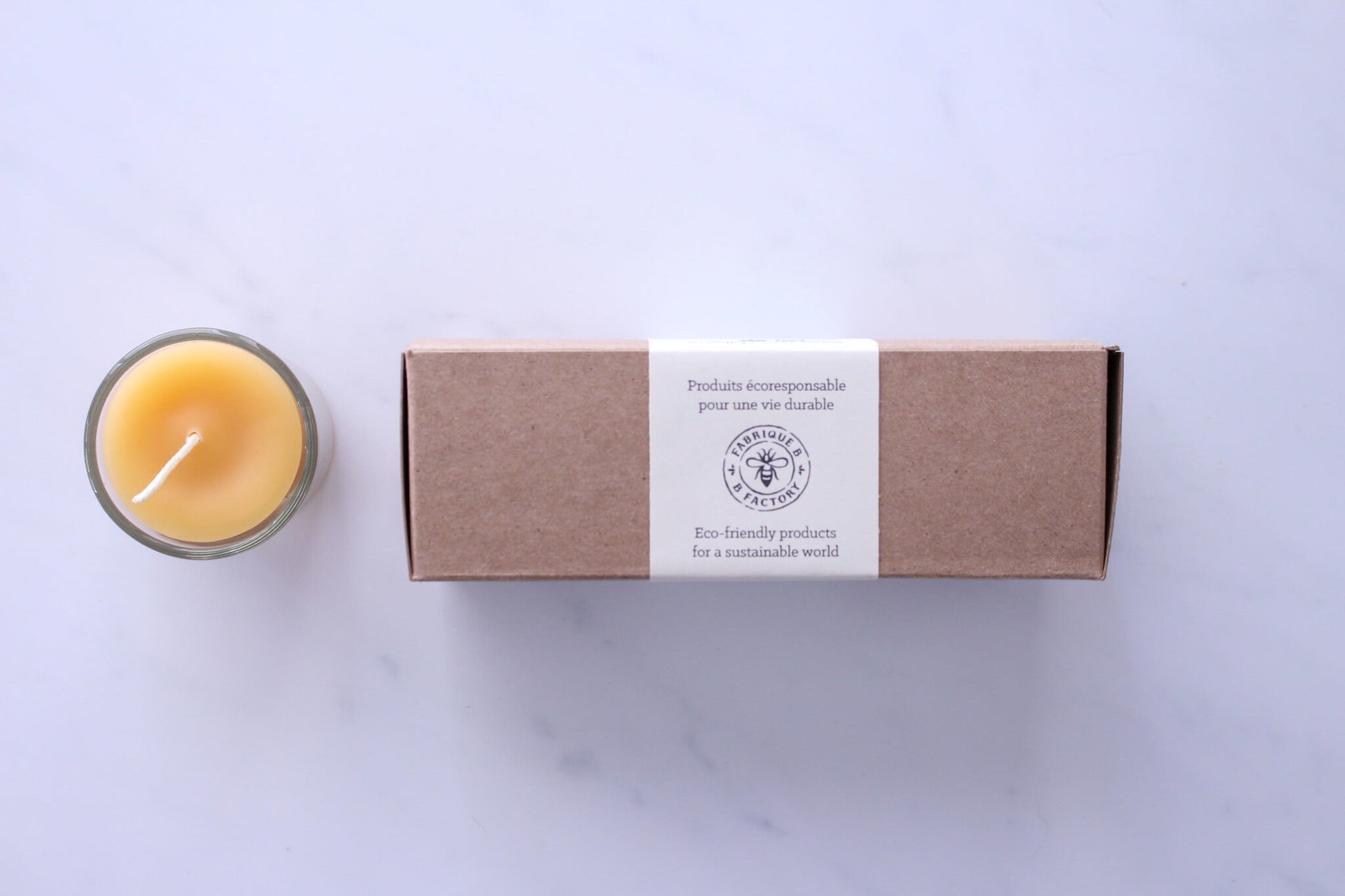 Pure beeswax votive candle in glass holder beside 3 beeswax votive candles in gift box with B Factory logo on lid 