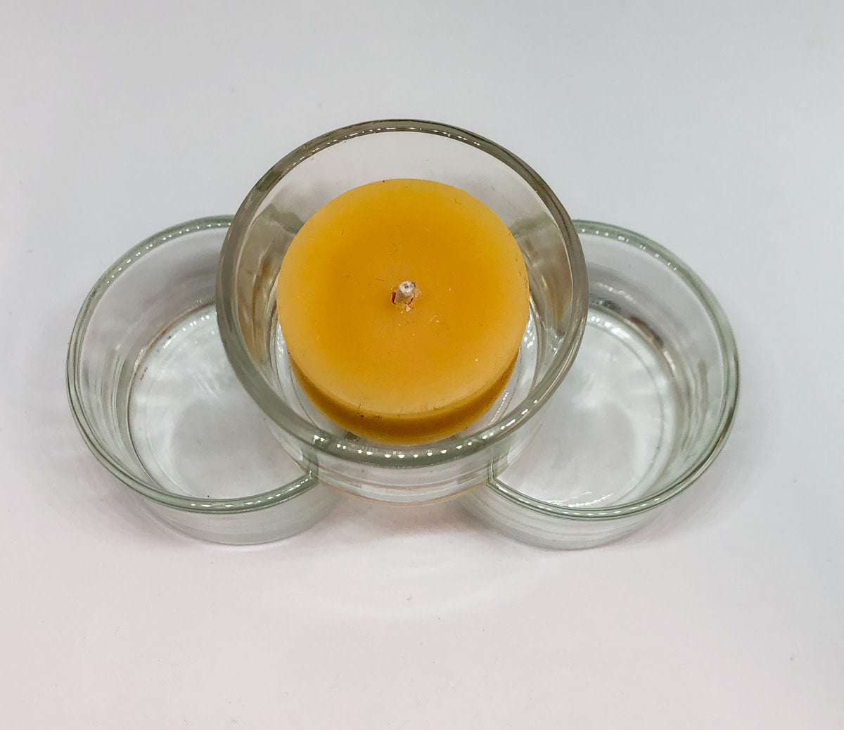Aerial view of beeswax tea light candle sitting on top of 2 empty clear glass tea light cups